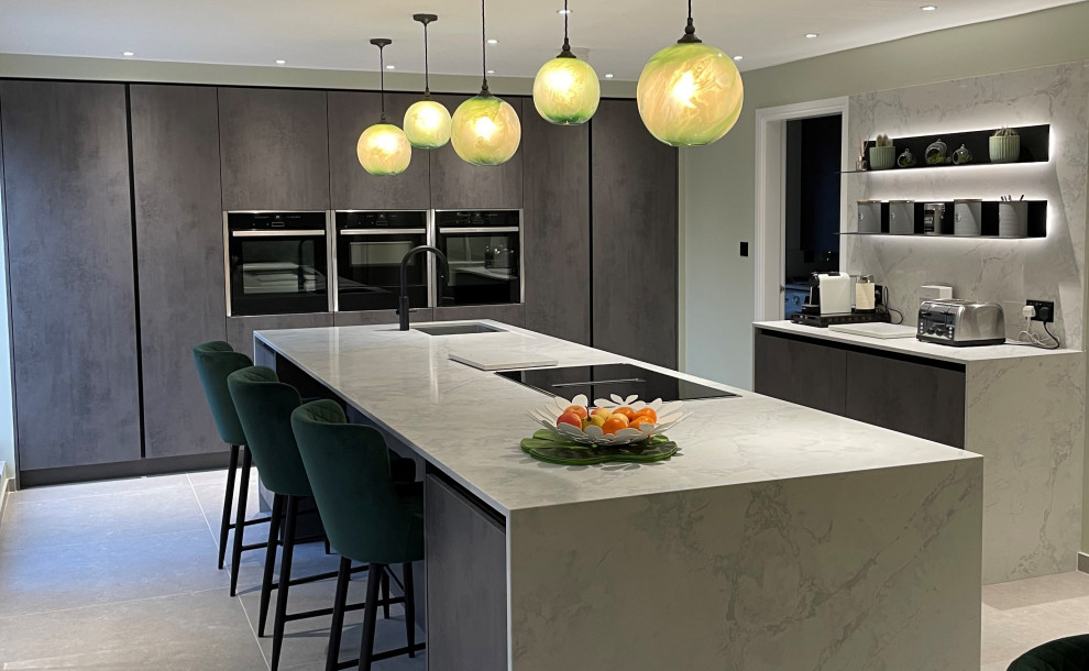 Photo of a large contemporary grey and white galley kitchen in Manchester with flat-panel cabinets, grey cabinets, quartz worktops, grey splashback, stainless steel appliances, porcelain flooring, an island, grey floors, grey worktops, a drop ceiling and a feature wall.