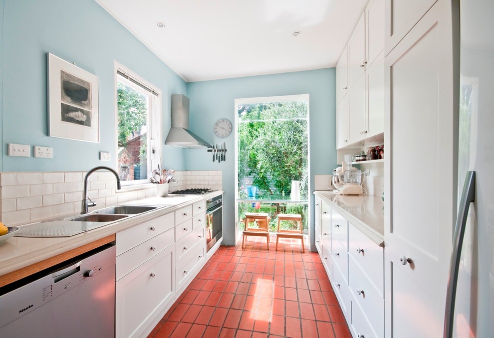 Mid-sized traditional galley kitchen in Melbourne with a double-bowl sink, recessed-panel cabinets, white cabinets, quartz benchtops, white splashback, ceramic splashback, stainless steel appliances, terra-cotta floors and no island.