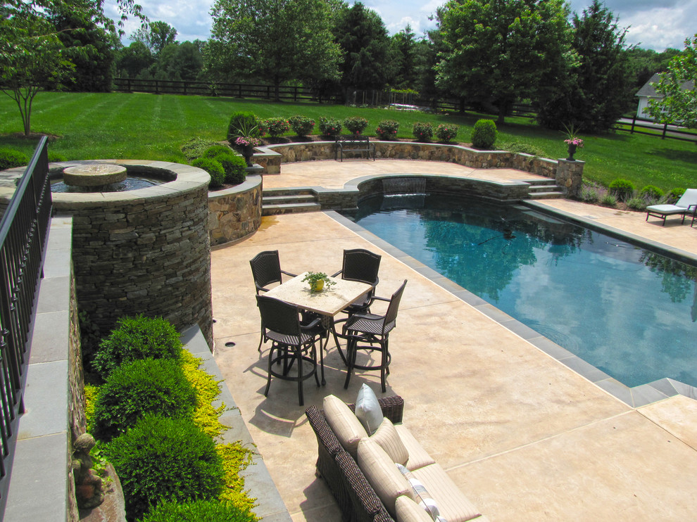This is an example of a large traditional backyard custom-shaped pool in DC Metro with a water feature and natural stone pavers.