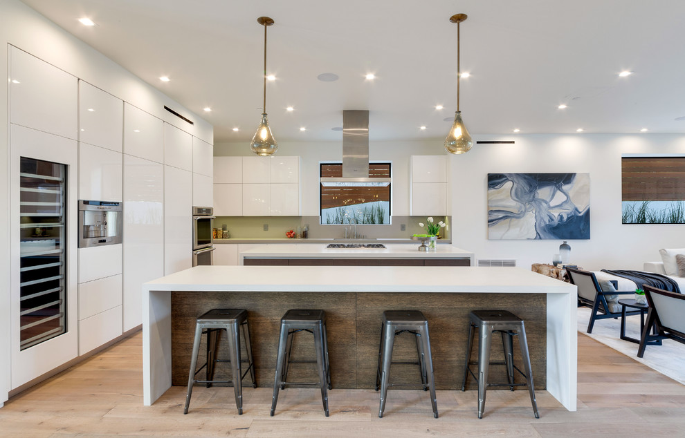 Inspiration for a contemporary open plan kitchen in Los Angeles with flat-panel cabinets, white cabinets, grey splashback, stainless steel appliances, light hardwood floors, multiple islands and beige floor.