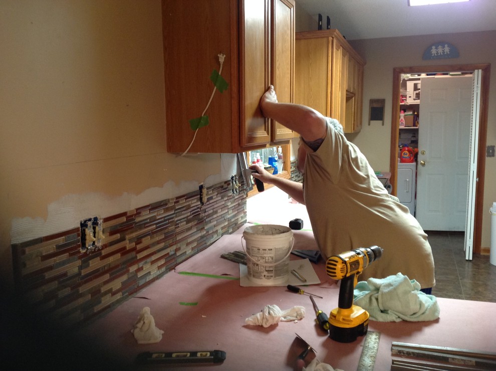 L-shaped eat-in kitchen photo with an undermount sink, flat-panel cabinets, brown backsplash, glass tile backsplash, stainless steel appliances and a peninsula