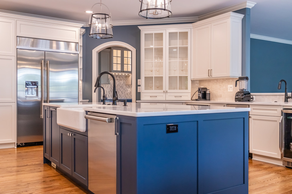 Large transitional u-shaped medium tone wood floor and brown floor eat-in kitchen photo in Baltimore with a farmhouse sink, shaker cabinets, blue cabinets, quartz countertops, white backsplash, marble backsplash, stainless steel appliances, an island and white countertops