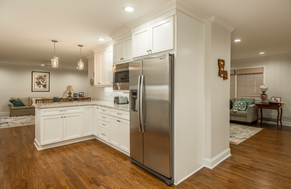 This is an example of a mid-sized l-shaped eat-in kitchen in Atlanta with a drop-in sink, recessed-panel cabinets, white cabinets, granite benchtops, white splashback, subway tile splashback, stainless steel appliances, medium hardwood floors, a peninsula, brown floor and yellow benchtop.