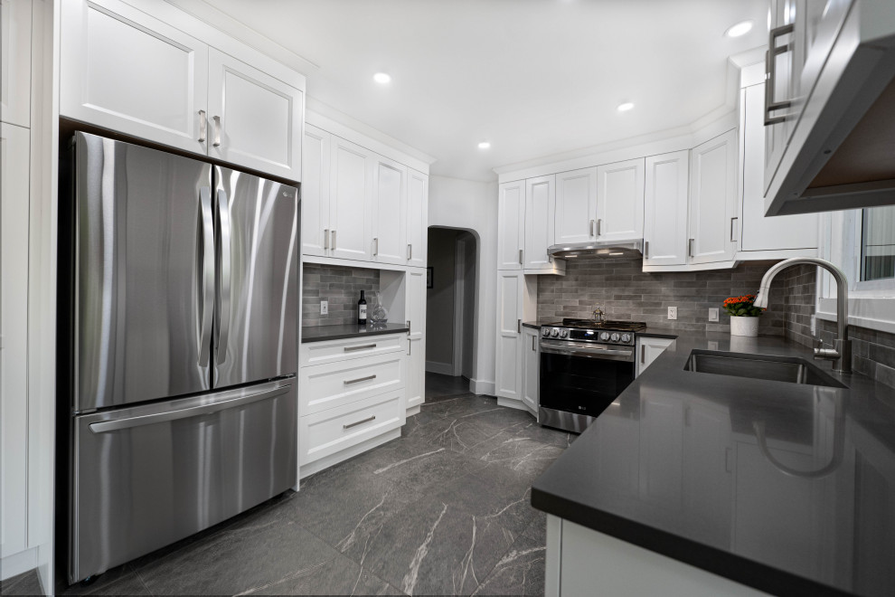 Example of a mid-sized transitional galley enclosed kitchen design with an undermount sink, shaker cabinets, white cabinets, quartz countertops, gray backsplash, subway tile backsplash, stainless steel appliances, no island and gray countertops
