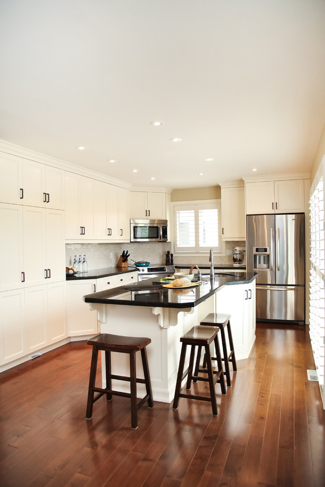Inspiration for a large traditional l-shaped eat-in kitchen in Toronto with a double-bowl sink, recessed-panel cabinets, white splashback, stainless steel appliances, granite benchtops, stone tile splashback, medium hardwood floors and with island.