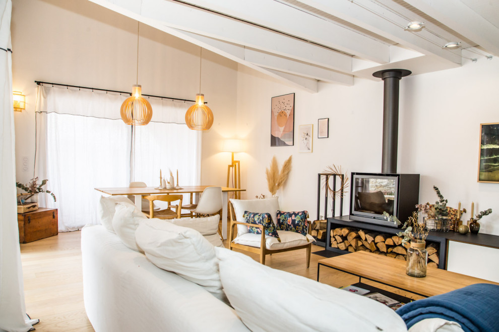 Идея дизайна: открытая гостиная комната в белых тонах с отделкой деревом в скандинавском стиле с белыми стенами, светлым паркетным полом, печью-буржуйкой и телевизором на стене