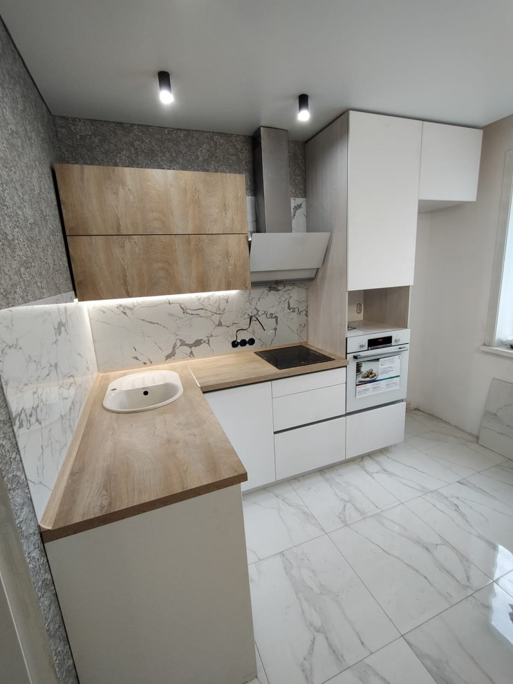 Design ideas for a small modern l-shaped open plan kitchen in Moscow with a built-in sink, flat-panel cabinets, white cabinets, wood worktops, white splashback, granite splashback, black appliances, ceramic flooring, no island, white floors and brown worktops.