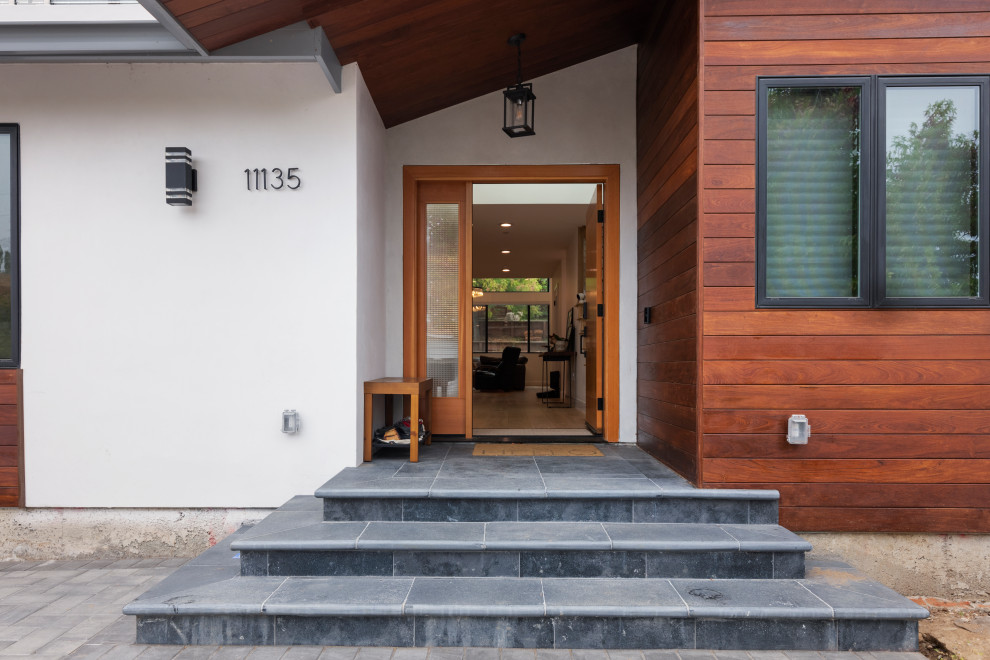 Réalisation d'une grande entrée minimaliste avec un mur gris, un sol en carrelage de porcelaine, une porte simple, une porte en bois clair et un sol gris.