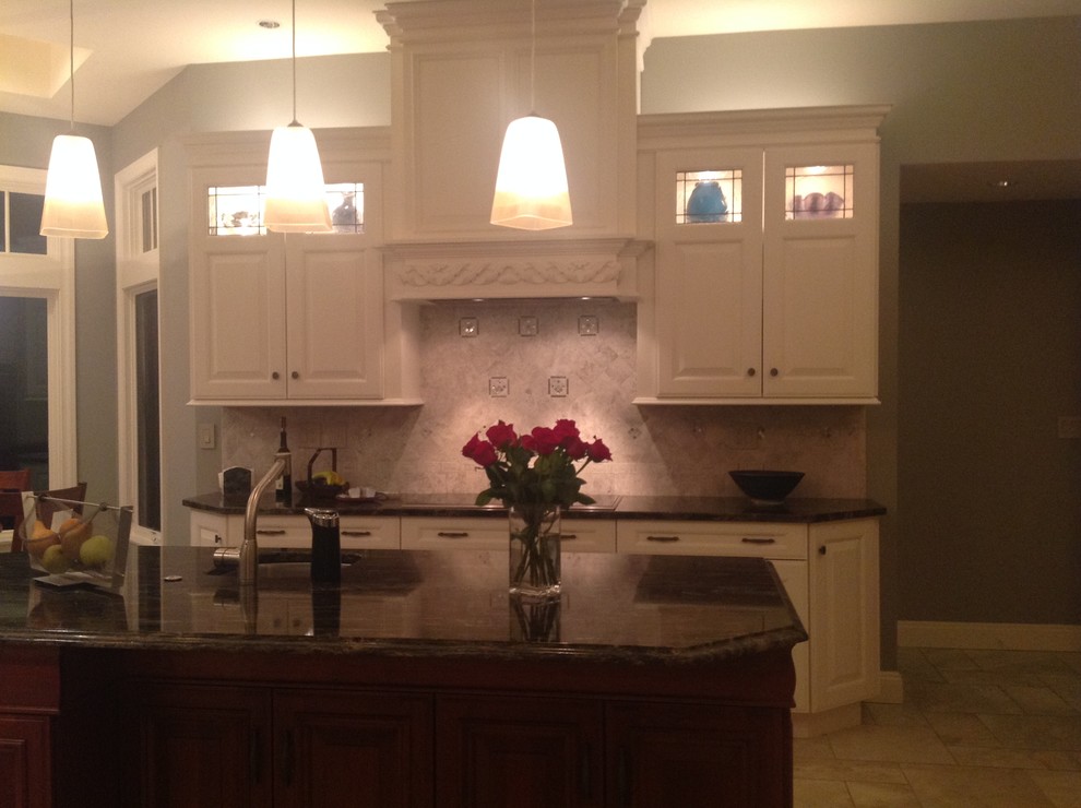 Inspiration for a mid-sized transitional u-shaped travertine floor eat-in kitchen remodel in New York with an undermount sink, raised-panel cabinets, white cabinets, granite countertops, beige backsplash, stone tile backsplash, stainless steel appliances and an island