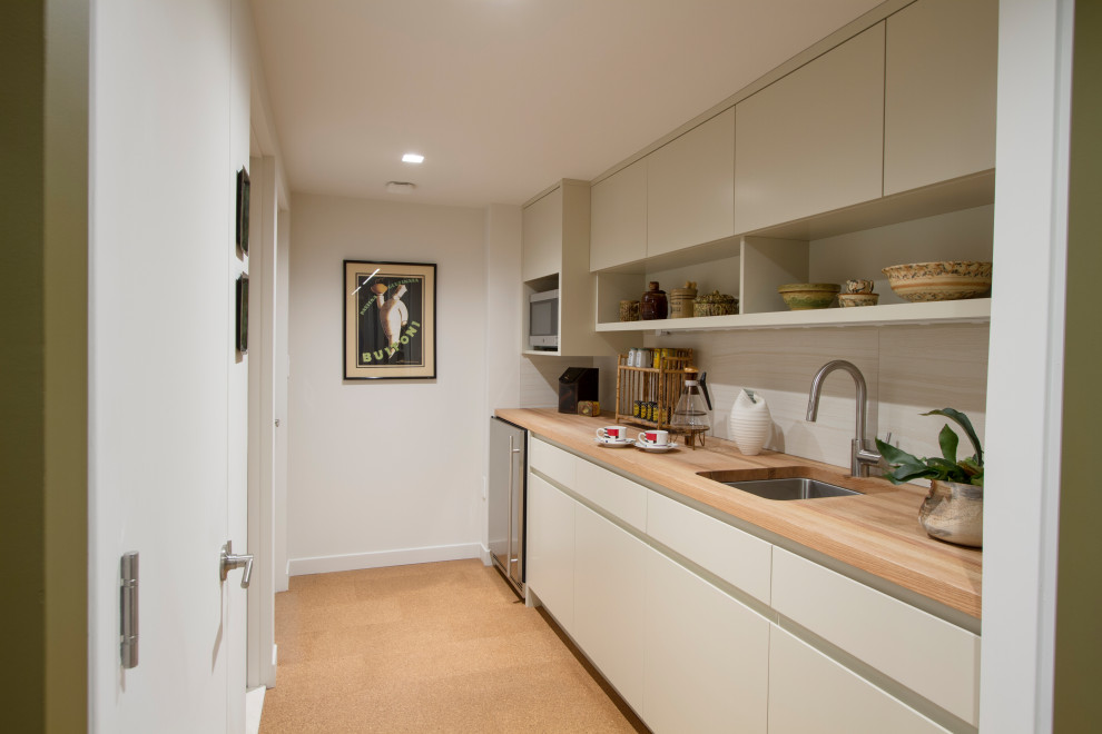 This is an example of a small modern galley kitchen pantry in New York with a submerged sink, flat-panel cabinets, white cabinets, wood worktops, beige splashback, porcelain splashback, stainless steel appliances, cork flooring, brown floors and brown worktops.