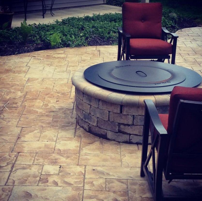 This is an example of a mid-sized country backyard patio in Cleveland with a fire feature, stamped concrete and no cover.