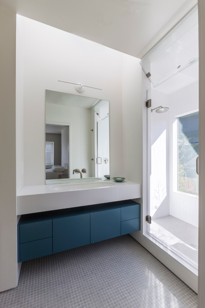 This is an example of a mid-sized contemporary master bathroom in San Francisco with blue cabinets, an alcove shower, a one-piece toilet, white walls, ceramic floors, limestone benchtops, an integrated sink, gray tile, ceramic tile and flat-panel cabinets.