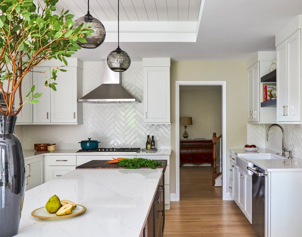 Example of a large transitional u-shaped light wood floor, brown floor and coffered ceiling eat-in kitchen design in Chicago with a farmhouse sink, shaker cabinets, white cabinets, quartz countertops, white backsplash, subway tile backsplash, stainless steel appliances, an island and multicolored countertops