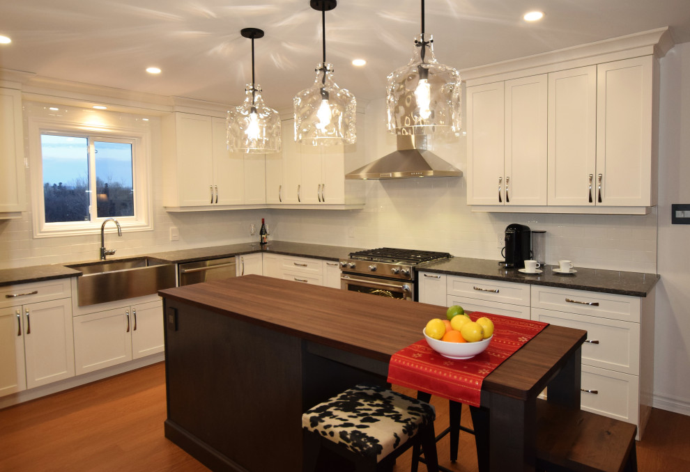 Example of a small transitional u-shaped medium tone wood floor and brown floor open concept kitchen design in Ottawa with a farmhouse sink, shaker cabinets, white cabinets, quartz countertops, white backsplash, subway tile backsplash, stainless steel appliances, an island and gray countertops