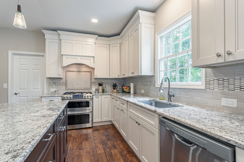 This is an example of a large traditional u-shaped open plan kitchen in Burlington with an integrated sink, shaker cabinets, beige cabinets, granite benchtops, beige splashback, ceramic splashback, stainless steel appliances, dark hardwood floors, with island, brown floor and beige benchtop.
