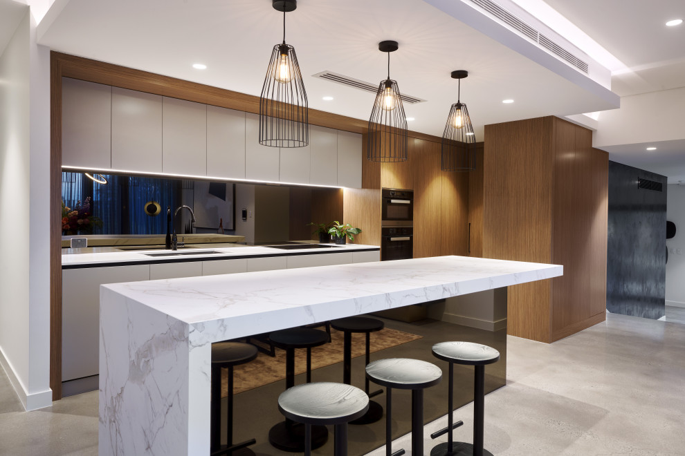 Inspiration for a large contemporary l-shaped kitchen in Perth with an undermount sink, flat-panel cabinets, white cabinets, black splashback, glass sheet splashback, panelled appliances, with island, grey floor and white benchtop.