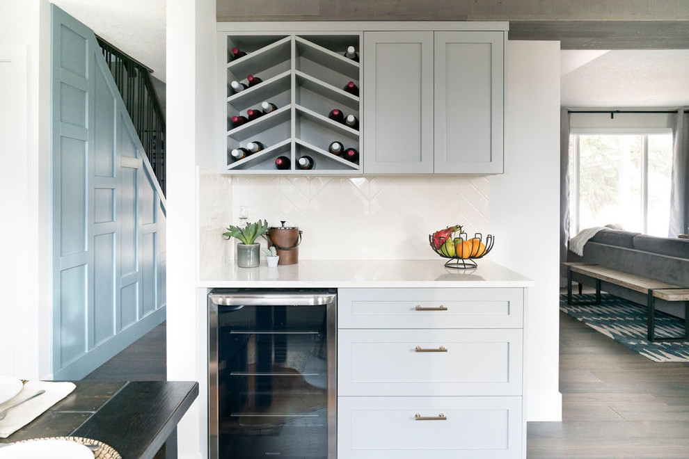 Photo of a small contemporary single-wall wet bar in Calgary with shaker cabinets, grey cabinets, quartz benchtops, white splashback, dark hardwood floors, brown floor and white benchtop.