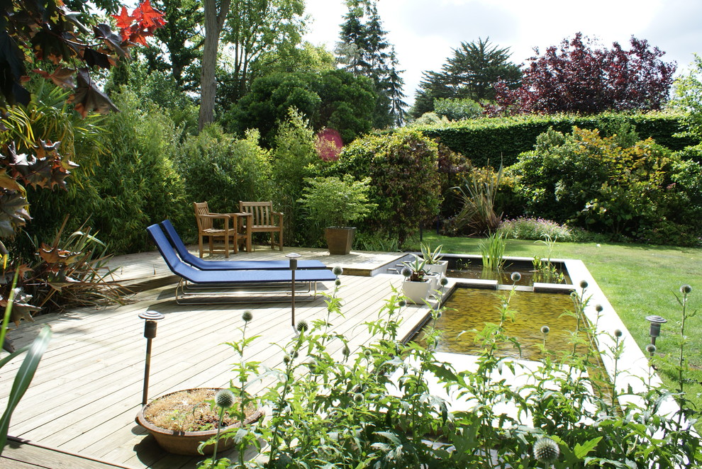 Large traditional backyard deck in Hertfordshire with a water feature and no cover.