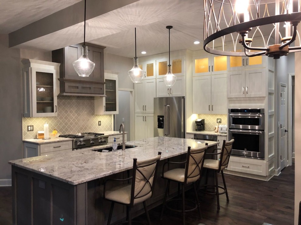 Photo of a large traditional l-shaped eat-in kitchen in Kansas City with an undermount sink, shaker cabinets, white cabinets, granite benchtops, grey splashback, ceramic splashback, stainless steel appliances, dark hardwood floors, with island, brown floor and multi-coloured benchtop.
