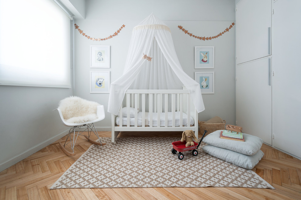 Contemporary gender-neutral nursery in Other with grey walls, light hardwood floors and beige floor.