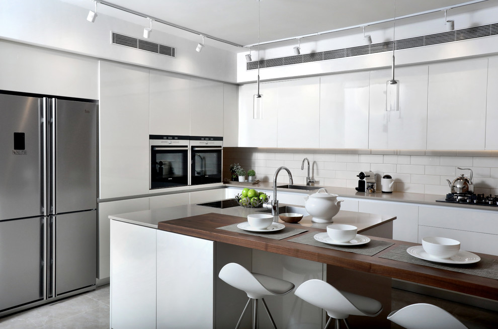 This is an example of a mid-sized modern l-shaped open plan kitchen with an undermount sink, flat-panel cabinets, white cabinets, quartz benchtops, white splashback, ceramic splashback, stainless steel appliances, porcelain floors and with island.