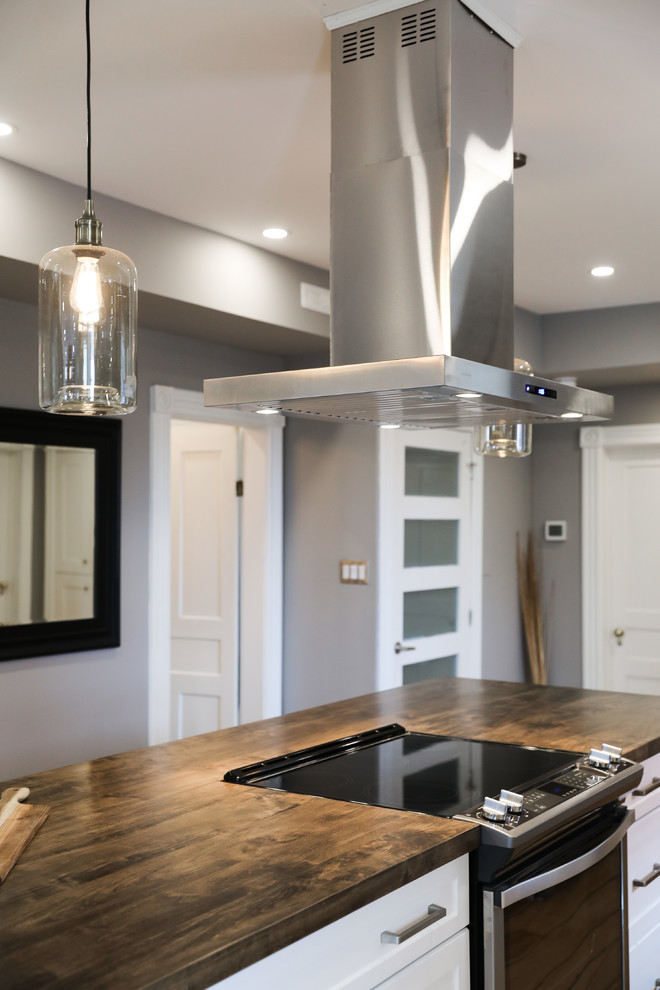 Mid-sized transitional single-wall medium tone wood floor and brown floor eat-in kitchen photo with a farmhouse sink, shaker cabinets, white cabinets, white backsplash, stainless steel appliances, an island and white countertops