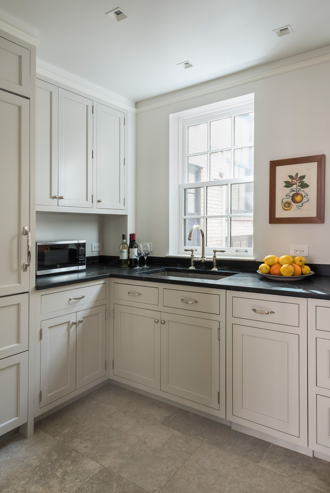Design ideas for a small traditional u-shaped kitchen in New York with an undermount sink, shaker cabinets, beige cabinets, soapstone benchtops, beige splashback, limestone splashback, panelled appliances, limestone floors and black benchtop.