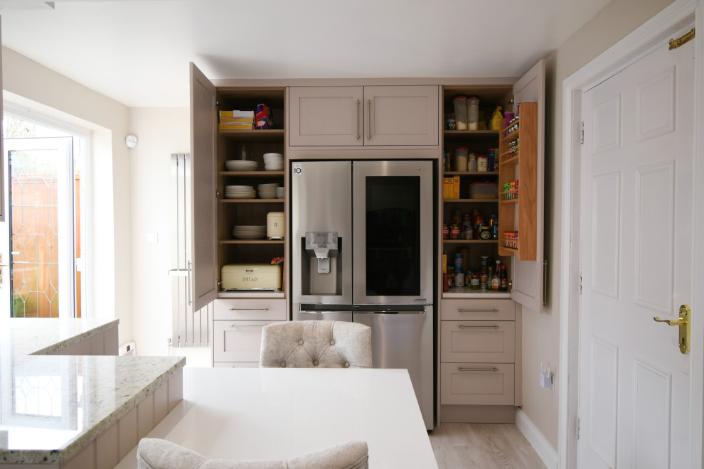 Inspiration for a medium sized classic l-shaped enclosed kitchen in Essex with a double-bowl sink, shaker cabinets, all types of cabinet finish, granite worktops, grey splashback, metal splashback, black appliances, laminate floors, a breakfast bar, white worktops and feature lighting.