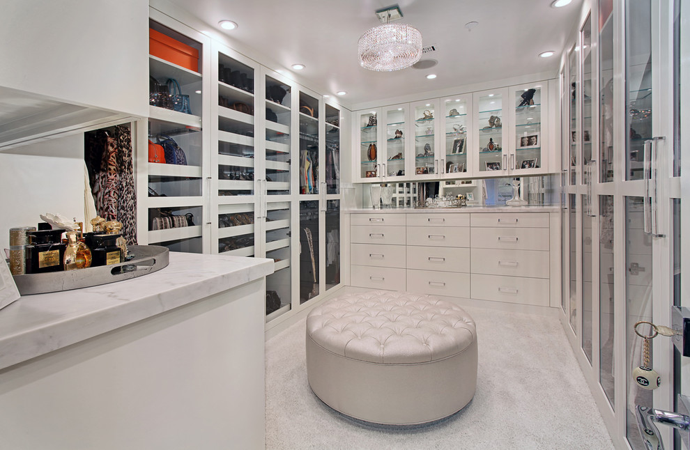 Large contemporary gender-neutral dressing room in Orange County with glass-front cabinets, white cabinets and carpet.