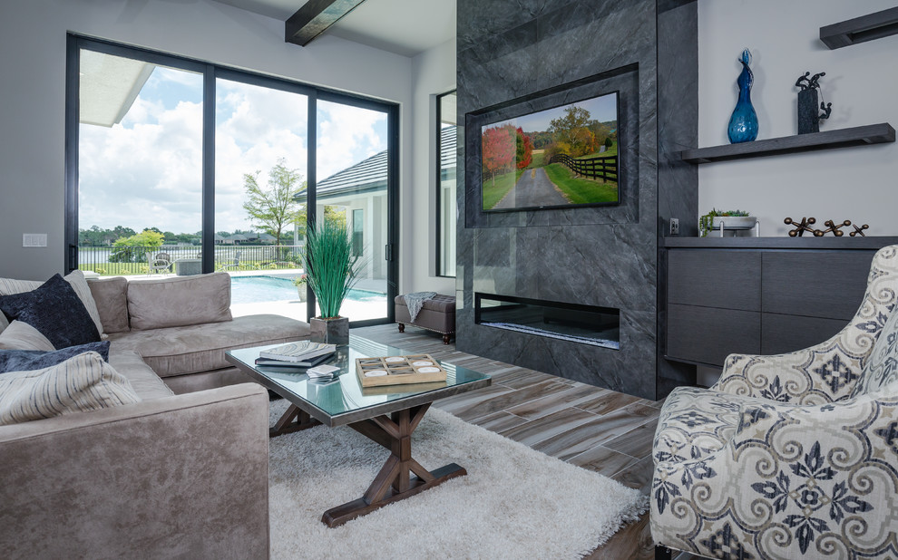 This is an example of a large contemporary open concept living room in Tampa with grey walls, porcelain floors, a standard fireplace, a tile fireplace surround, a wall-mounted tv and multi-coloured floor.