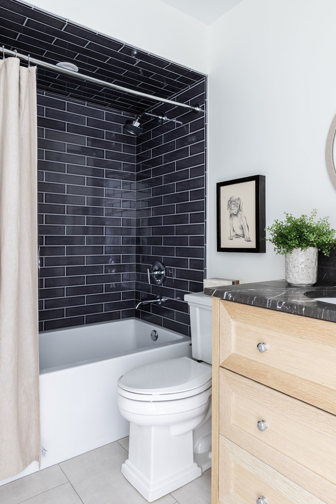 Photo of a mid-sized country 3/4 bathroom in Chicago with furniture-like cabinets, light wood cabinets, an alcove tub, a shower/bathtub combo, a two-piece toilet, white walls, porcelain floors, an undermount sink, marble benchtops, grey floor, a shower curtain and black benchtops.