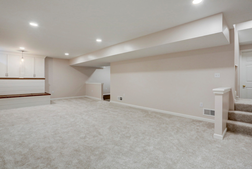 This is an example of a large arts and crafts look-out basement in Philadelphia with beige walls, carpet and white floor.