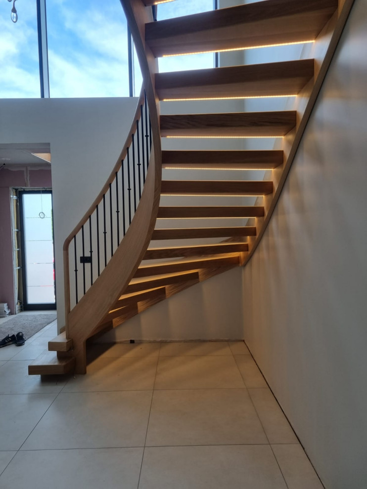 Large contemporary wood curved metal railing staircase in West Midlands with open risers.