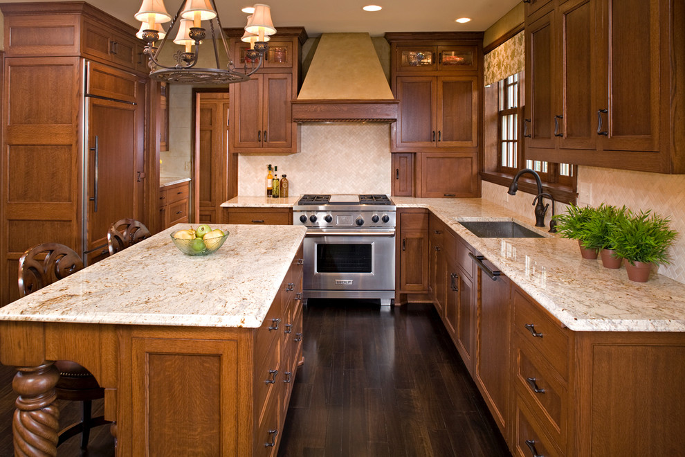 Photo of a large traditional l-shaped eat-in kitchen in Minneapolis with an undermount sink, medium wood cabinets, granite benchtops, beige splashback, stone tile splashback, panelled appliances, dark hardwood floors and with island.