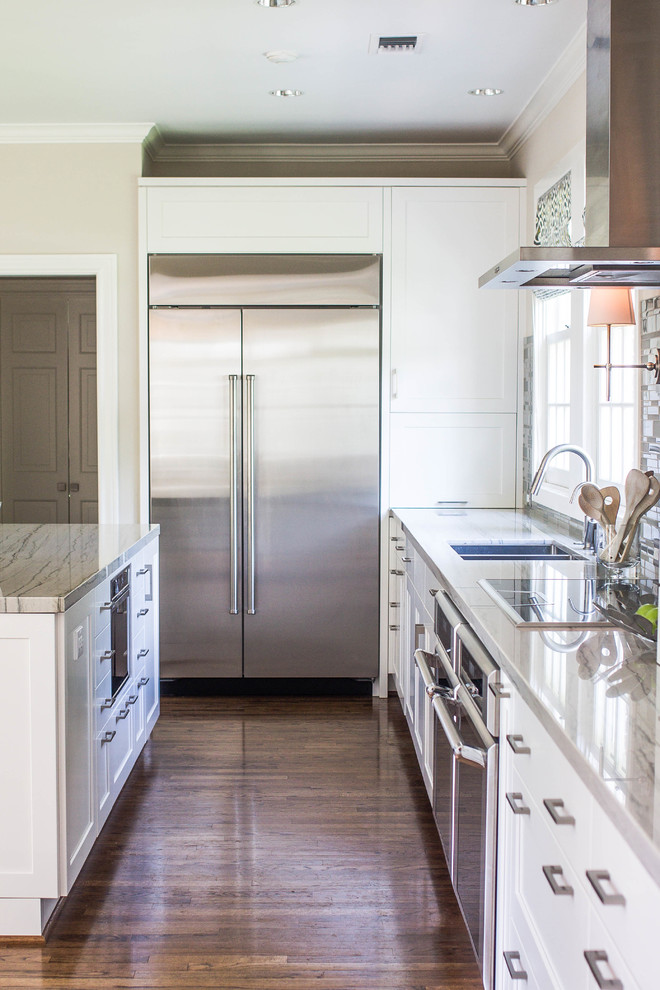 Inspiration for a large transitional l-shaped dark wood floor open concept kitchen remodel in Houston with a double-bowl sink, shaker cabinets, white cabinets, quartzite countertops, gray backsplash, glass tile backsplash, stainless steel appliances and an island