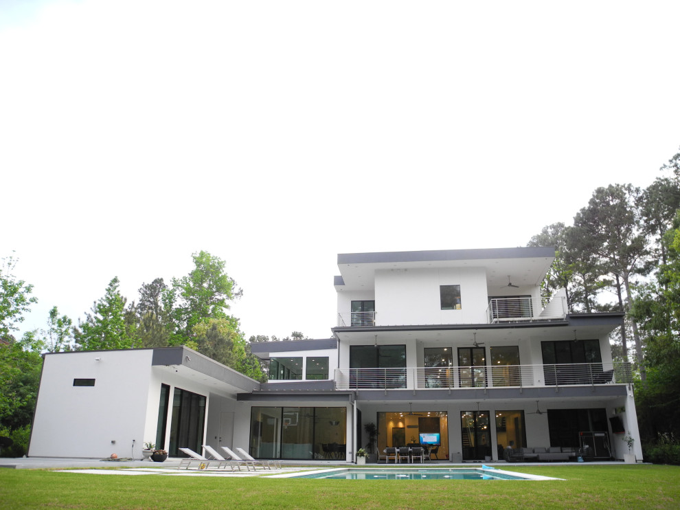 На фото: огромный, трехэтажный, белый частный загородный дом в стиле модернизм с облицовкой из цементной штукатурки, плоской крышей, металлической крышей и белой крышей