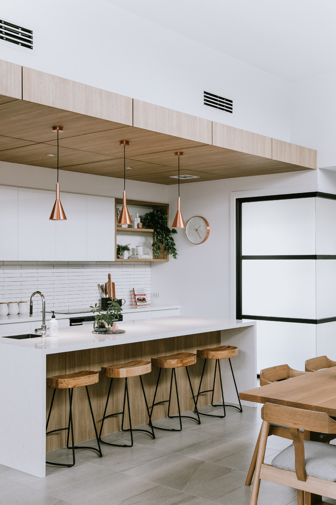 Design ideas for a large contemporary galley eat-in kitchen in Other with an undermount sink, flat-panel cabinets, white cabinets, white splashback, matchstick tile splashback, with island, grey floor and white benchtop.