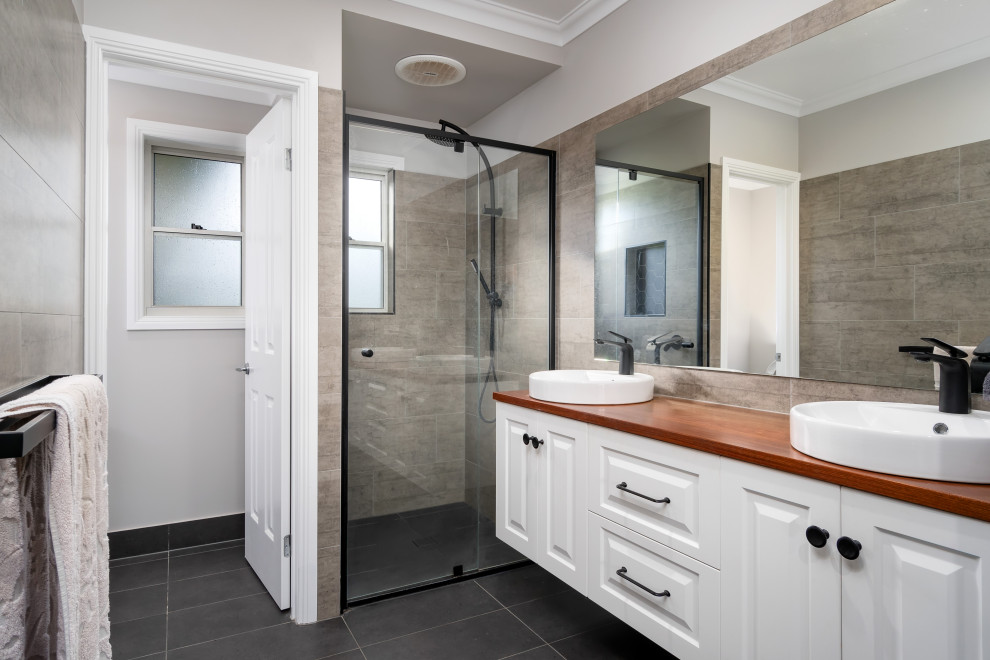 Photo of a large transitional 3/4 bathroom in Other with raised-panel cabinets, white cabinets, an alcove shower, gray tile, grey walls, a vessel sink, wood benchtops, black floor, a hinged shower door, brown benchtops, a double vanity and a floating vanity.