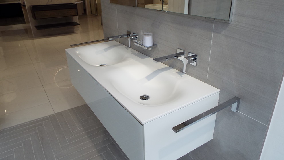 Photo of a contemporary bathroom in London with glass-front cabinets, white cabinets, a freestanding bath, a walk-in shower, a wall mounted toilet, grey tiles, porcelain tiles, grey walls, porcelain flooring, an integrated sink, engineered stone worktops, grey floors, an open shower and white worktops.