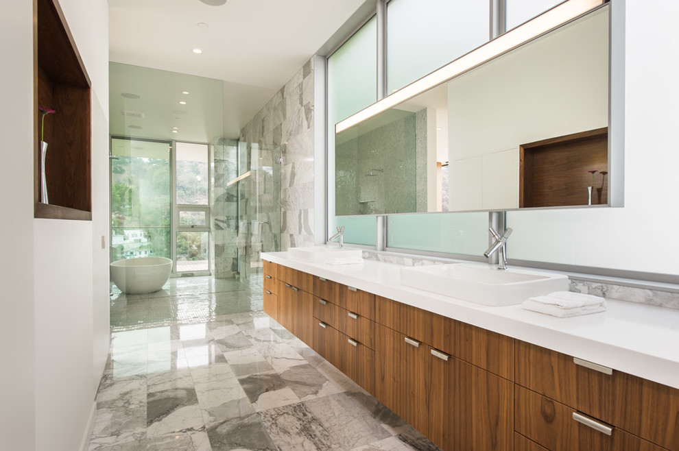 Inspiration for an expansive contemporary master bathroom in Los Angeles with flat-panel cabinets, dark wood cabinets, a freestanding tub, white walls, an open shower, a one-piece toilet, gray tile, stone tile, marble floors, an undermount sink and engineered quartz benchtops.