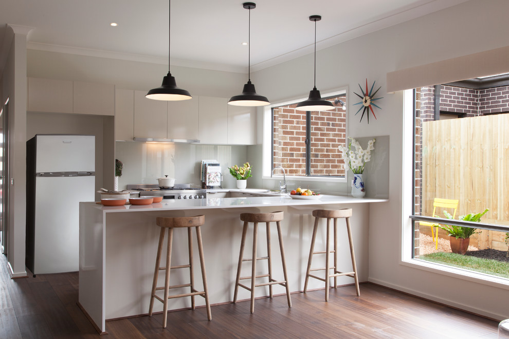 Photo of a mid-sized contemporary u-shaped eat-in kitchen in Melbourne with flat-panel cabinets, white cabinets, laminate benchtops, grey splashback, glass sheet splashback, stainless steel appliances, medium hardwood floors and a peninsula.