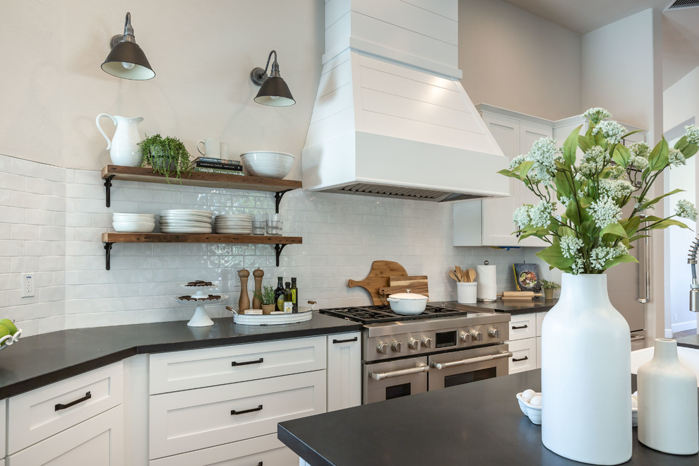 Inspiration for a transitional l-shaped medium tone wood floor and brown floor kitchen remodel in Phoenix with shaker cabinets, white cabinets, white backsplash, stainless steel appliances, an island and black countertops