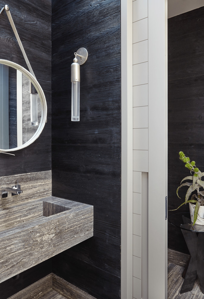 Photo of a beach style powder room in New York with black walls, a wall-mount sink, travertine floors, travertine benchtops, black floor and black benchtops.