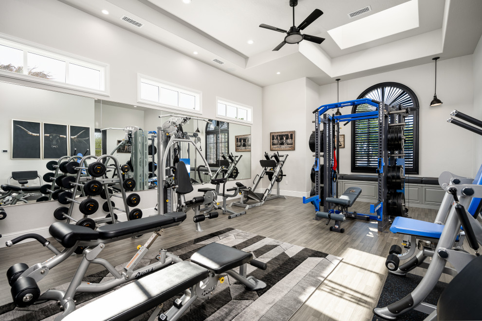 Imagen de sala de pesas moderna extra grande con paredes blancas, suelo de madera clara, suelo marrón y casetón