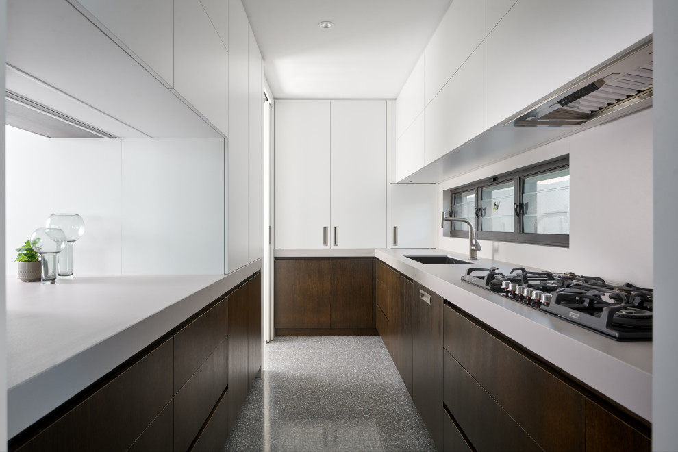 This is an example of an expansive contemporary l-shaped eat-in kitchen in Perth with an undermount sink, flat-panel cabinets, white cabinets, quartz benchtops, white splashback, porcelain splashback, black appliances, concrete floors, with island, grey floor and white benchtop.