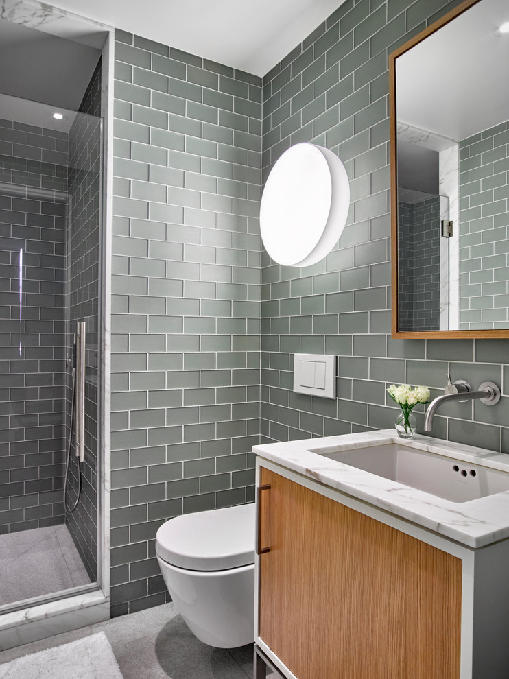 This is an example of a contemporary kids bathroom in New York with flat-panel cabinets, medium wood cabinets, an alcove shower, a wall-mount toilet, marble floors, an undermount sink, marble benchtops, gray tile and subway tile.