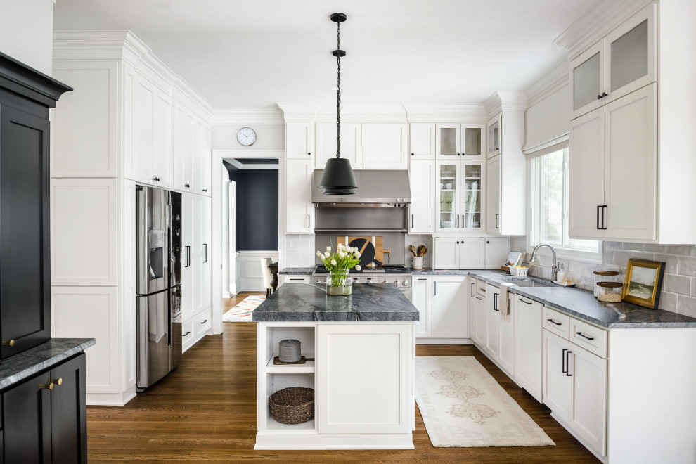 This is an example of a mid-sized transitional l-shaped eat-in kitchen in Charlotte with an undermount sink, shaker cabinets, white cabinets, quartzite benchtops, grey splashback, porcelain splashback, stainless steel appliances, medium hardwood floors, with island, brown floor and black benchtop.