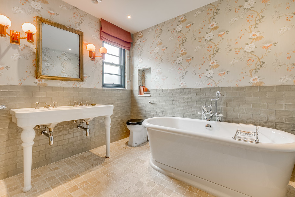 Photo of a mid-sized traditional master bathroom in London with a freestanding tub, gray tile, stone tile, a console sink, beige floor, white benchtops and a one-piece toilet.