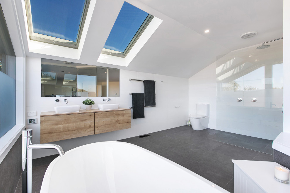 Idées déco pour une salle de bain moderne en bois clair avec une baignoire indépendante, un carrelage blanc, un mur blanc, un sol en carrelage de céramique, un plan de toilette en bois, un sol gris, meuble double vasque et meuble-lavabo suspendu.