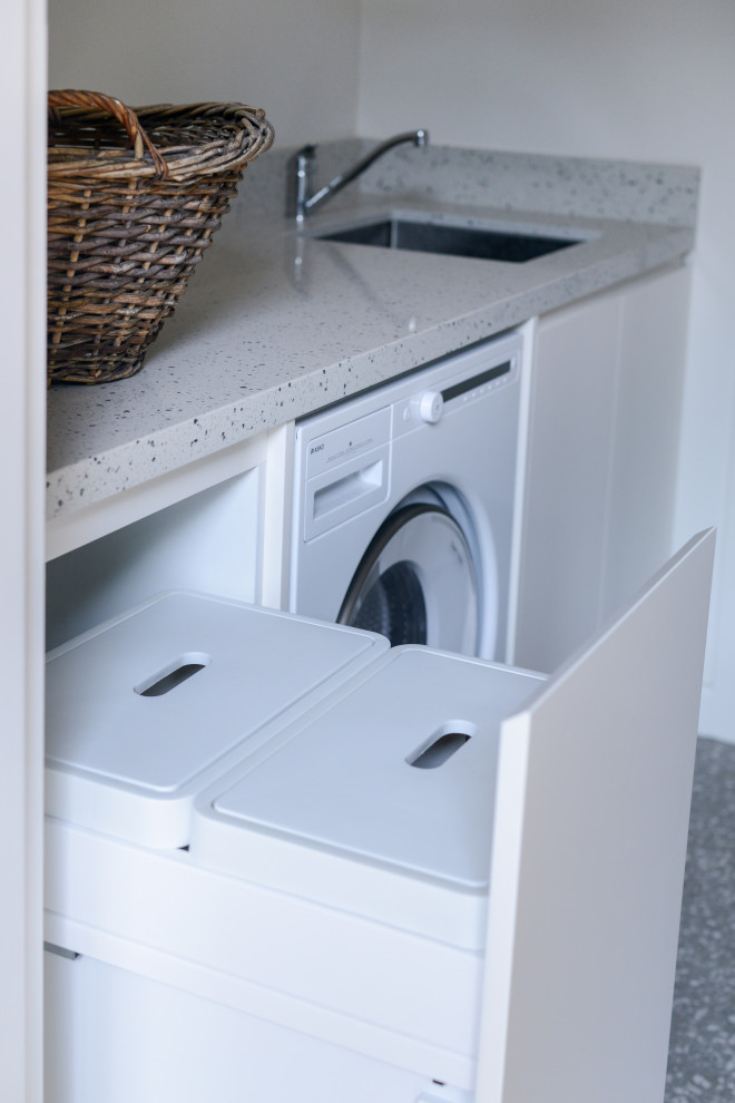 Photo of a mid-sized modern single-wall dedicated laundry room in Sydney with a drop-in sink, flat-panel cabinets, beige cabinets, quartz benchtops, beige walls, terra-cotta floors, grey floor and beige benchtop.